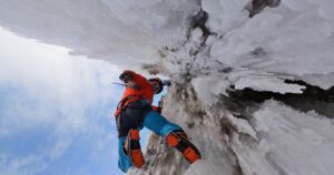 an ice climber on an icy rock wall looking down at the camera
