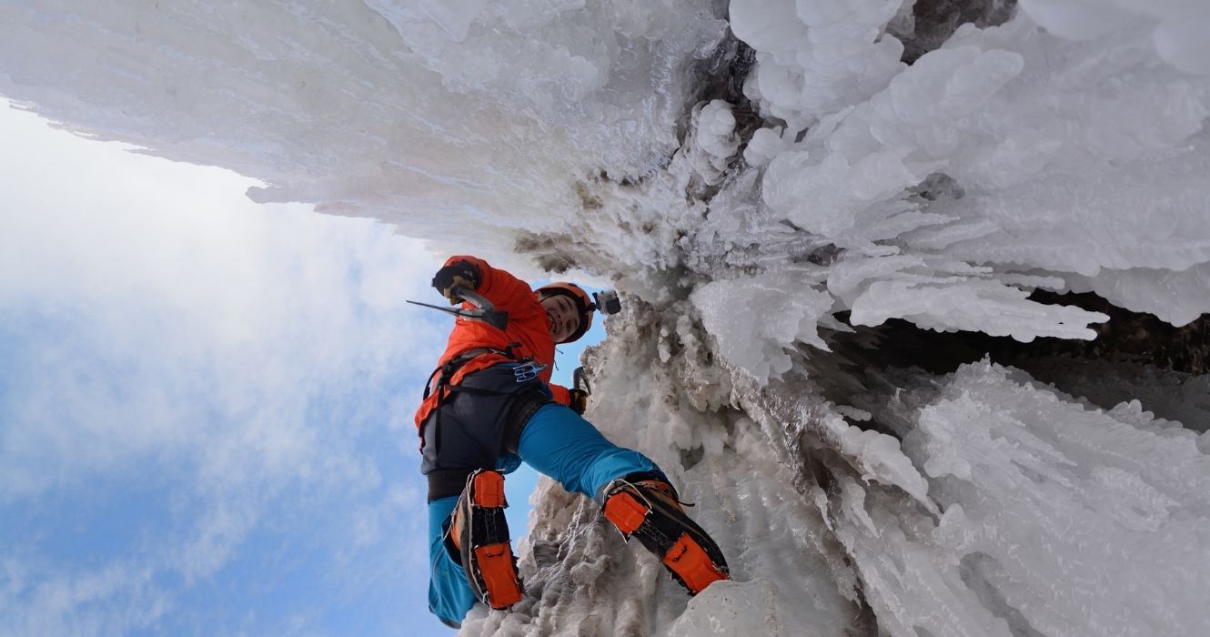 um alpinista de gelo em uma parede de rocha gelada olhando para a câmera