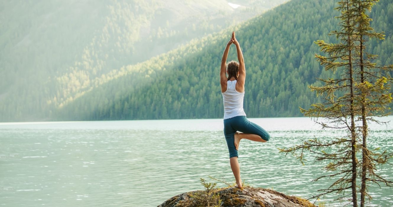 uma mulher praticando ioga nas montanhas perto de um lago