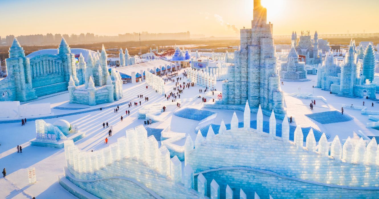 esculturas de gelo e edifícios com o nascer do sol ao fundo no festival de gelo e neve de Harbin