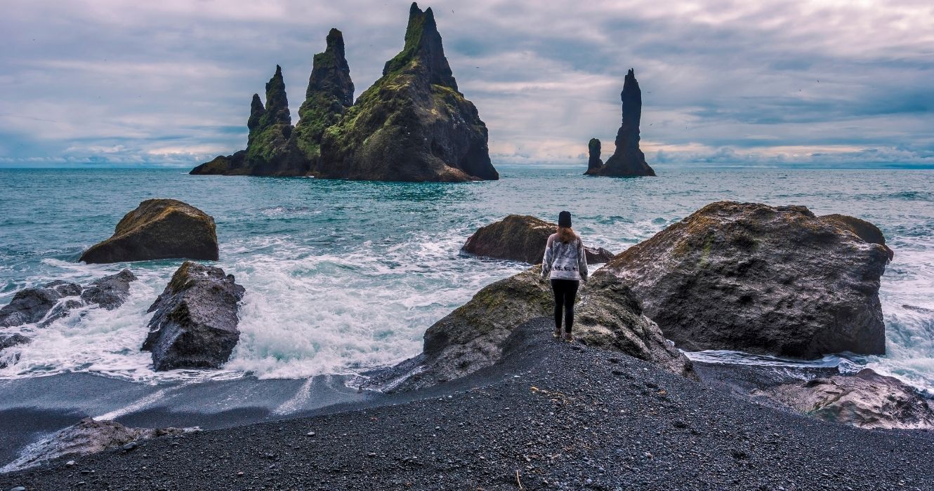 uma mulher em pé na praia de reynisfjara, na islândia