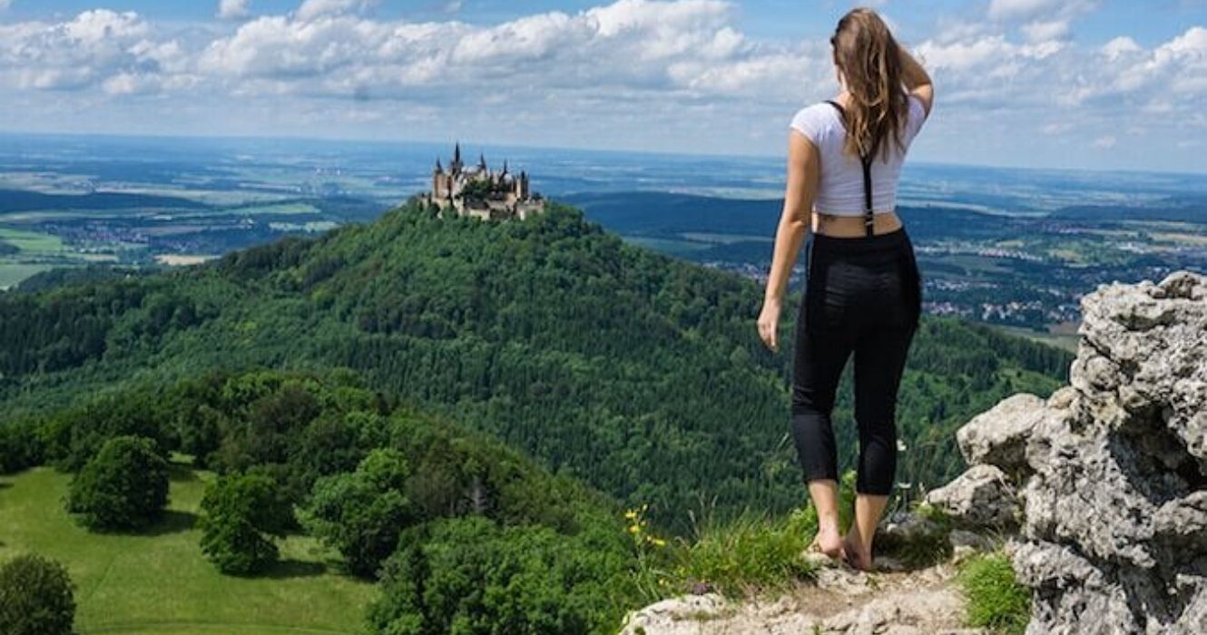 uma garota fica no topo de um penhasco com vista para um castelo