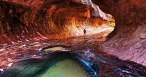 a hiker trekking through the water in slot canyon at zion national park